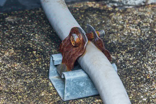 Rusty metal clamp holding electrical conduit on rooftop. photo