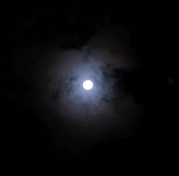 Close up detail of the full moon shining through the bluish clouds photo