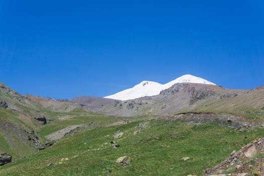 mountain landscape, stream in green highland valley with snowy peak of Mount Elbrus in the distance photo