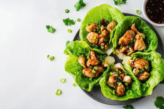 A plate of lettuce wraps filled with chicken and sauce, garnished with green onions. photo