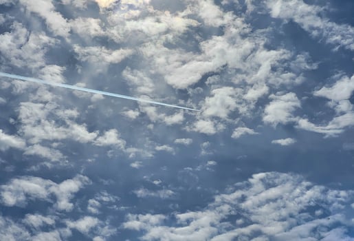A white trail in the blue sky with small white clouds from the plane photo