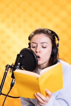 Woman sings, doing voiceover reading of kids book to produce audiobook using dramatic acting. Narrator using storytelling skills and melodious voice while recording children novel, studio background photo
