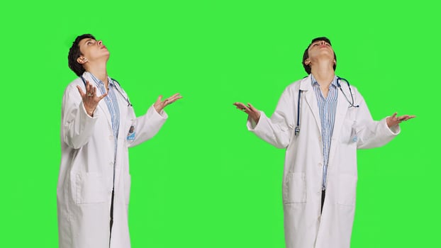 Religious woman physician praying to jesus christ against greenscreen, looking up and saying a prayer. Doctor worshipping God and meditating, spiritual medic with belief in christianity. Camera B. photo