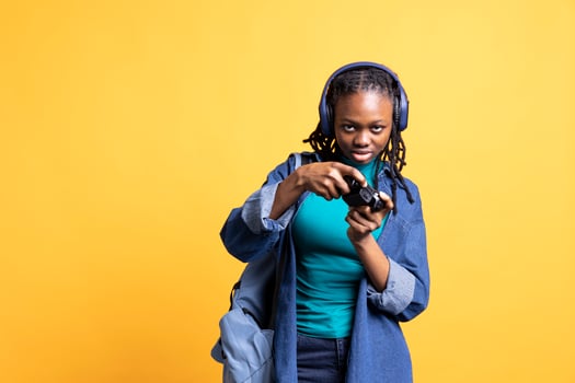 African american gamer holding controller, focused on finishing videogame level, wearing headphones. Woman gaming with gamepad, solving quests, isolated over yellow studio backdrop photo