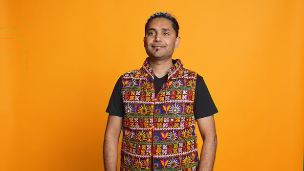 Portrait of optimistic indian man wearing colorful vest with positive facial expression smiling, looking pleased. Calm person in traditional clothing, feeling satisfied, studio backdrop, camera B photo