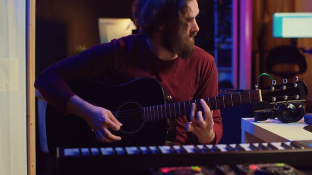 Artist working with daw software at his home studio to record new music on mixing console and soundboard, audio engineering. Musician playing song on guitar and adjusting volume. Camera A. photo