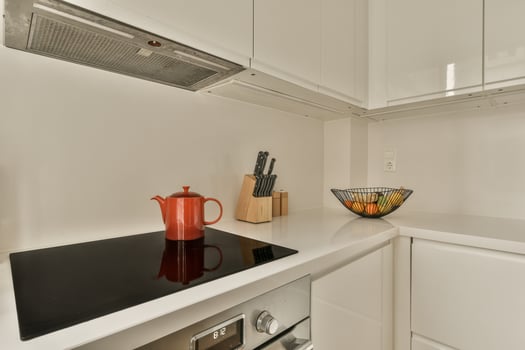A white kitchen with a red kettle and a bowl photo
