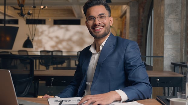 Arabian Indian man ethnic businessman employee manager analyst male office worker writing tasks business plan paperwork write notes signing documents happy joyful guy looking camera smile at workplace photo