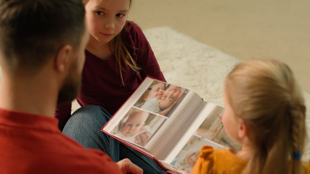 Caucasian parent father and children kids laughing having fun together enjoy evening weekend happy dad daughters babies siblings little girls hold book with funny photos watching family photo album