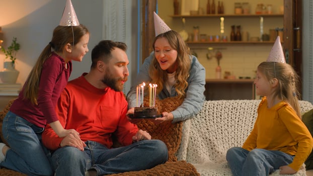 Happy birthday event Caucasian family mom children congratulate dad surprise birth party cheerful parents little girls kids daughters siblings festive caps celebrate blowing candles cake together home photo