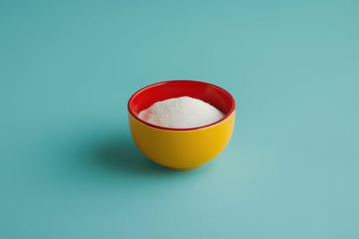 Bowl of white sugar on a turquoise background with a red rim photo