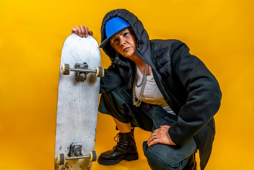 beautiful middle aged woman in black hoodie poses as rapper playing with skateboard on colorful background photo