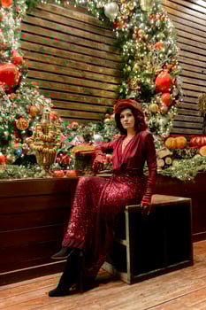 A woman in a red dress sits on a wooden crate in front of a Christmas tree photo