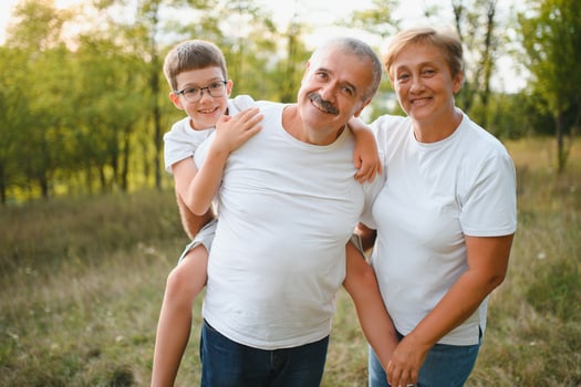 Grandson, grandfather and grandmother sitting on grass having fun outdoors in park at sunset photo