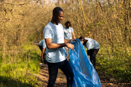 African american person collecting garbage in a bag for community service, contributing to litter cleanup project. Young activist preserving and clearing the natural forest ecosystem. photo