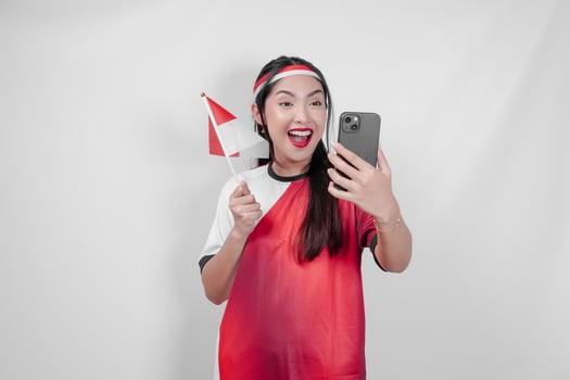 Attractive Indonesian woman holding a mini flag while watching sport competition through phone. photo