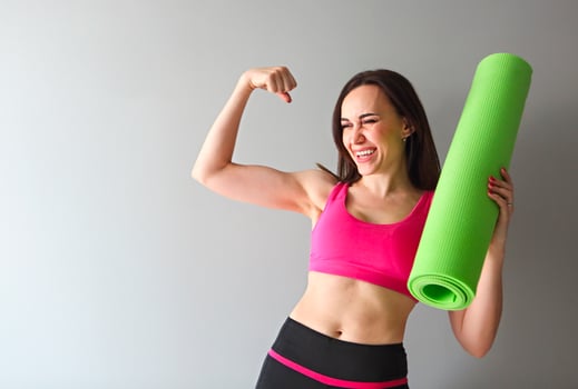 Attractive woman wearing pink sportswear holding green yoga or fitness mat after working out at home or in club photo