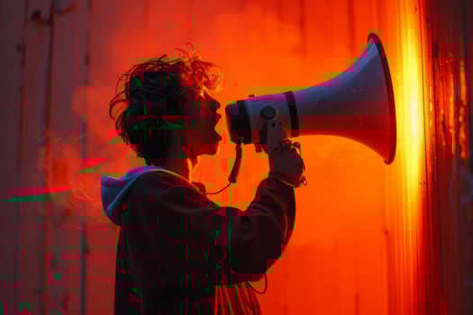 Young man shouting into megaphone with red light in background photo