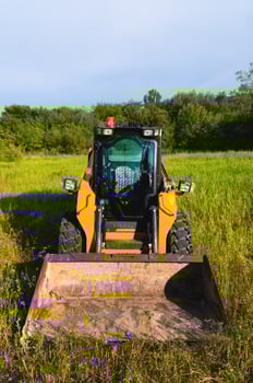 Small bulldozer will level the ground, preparing for new housing construction. Construction equipment on green grass in a field photo