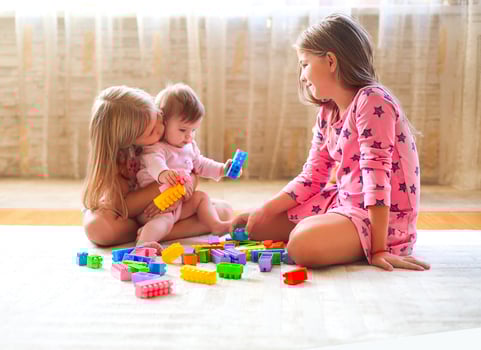 Three little blond girls playing with lots of colorful toy blocks indoor photo