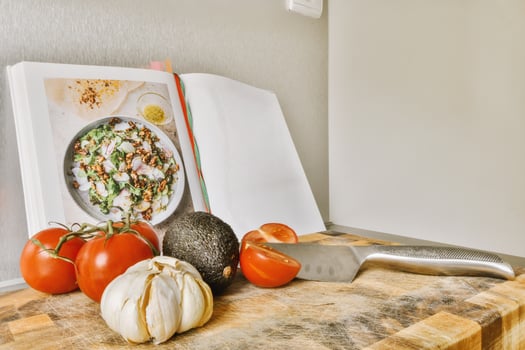 A book on a cutting board with tomatoes, garlic, and a knife photo