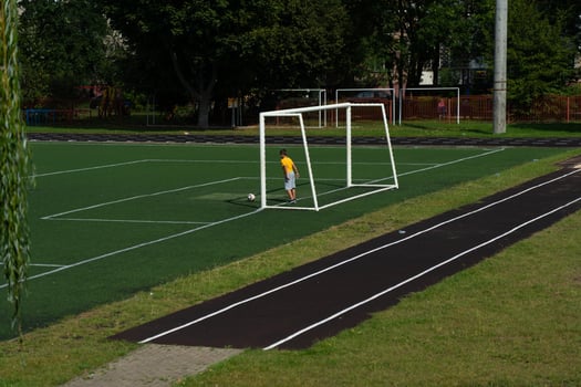A schoolboy, a football player hits the ball are standing in the goal. Stadium photo