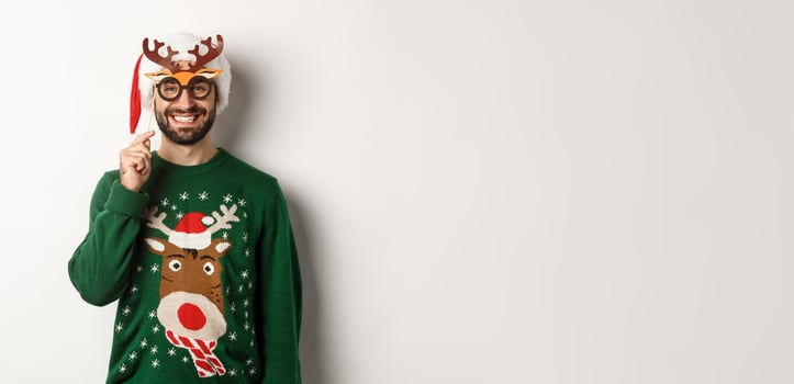 Christmas and holidays concept. Smiling beared man in Santa hat looking happy, holding party mask for New Year, celebrating xmas, standing over white background photo