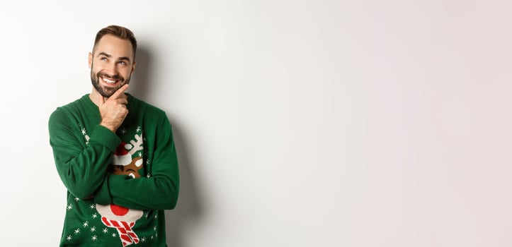 New year celebration and winter holidays concept. Thoughtful nice guy thinking about Christmas gifts, looking at upper left corner and smiling, white background photo