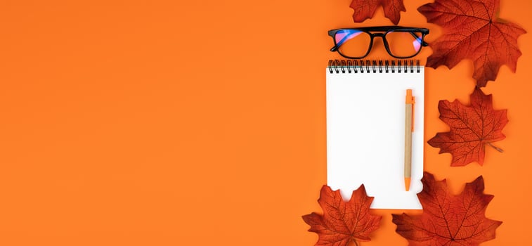 Autumn composition with blank notepad, pen, glasses and autumn leaves on orange background. Banner. Top view. Flatlay. Place for text. photo