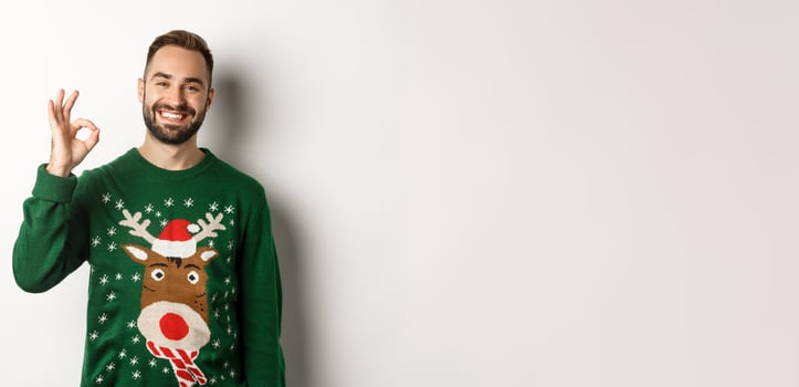 Winter holidays and christmas. Happy bearded man showing okay sign and smiling, approve or agree, praising something good, standing over white background photo