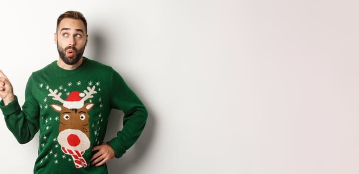 Winter holidays and christmas. Man looking curious at New Year shopping promo, standing in funny sweater against white background photo
