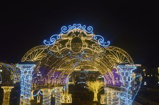 Festive Christmas illumination - bright glowing decorative arch against the night sky. New Year's city street decor. photo