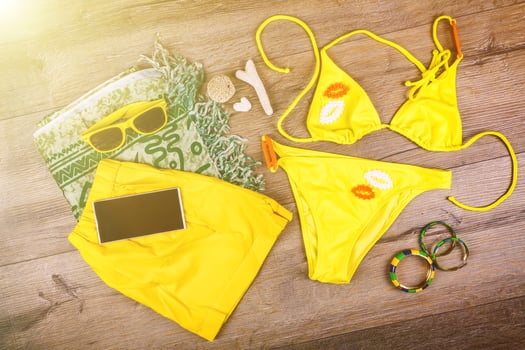 Set of beach clothes yellow bikini, bracelets, shorts, glasses on dark wooden background. Top view. Summer Holiday Concept. photo