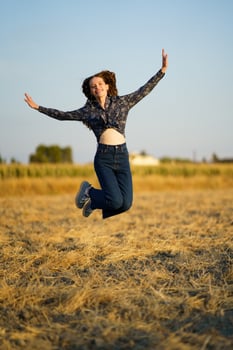 Joyful Young Woman Happily Jumping in a Beautiful Sunny Field Filled with Green Grass photo