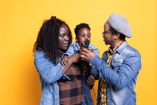 African american parents teaching their cute toddler to sing on microphone, learning to perform melody from a young age. Sweet talented small boy singing music in front of the camera. photo
