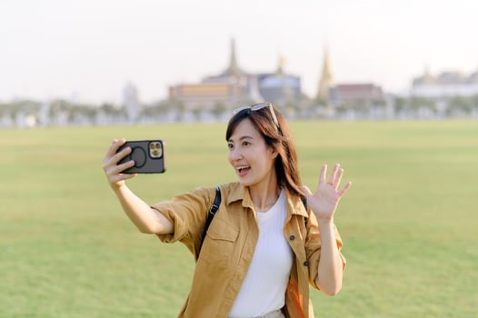 Traveler asian woman in her 30s making a livestream or selfie on smartphone while explores Wat Phra Kaew emerald Buddha. Share the wonders of Thai heritage through her journey. photo