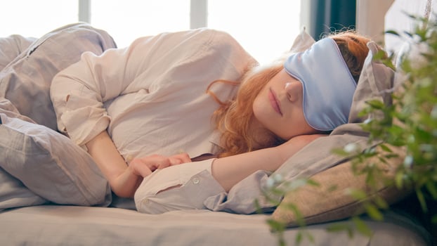 Lazy Caucasian girl with blindfold in bed in morning woman sleeping napping during daytime sleepy female waking up lying in comfortable bed peeks out from under sleep mask opens eye fall asleep again photo
