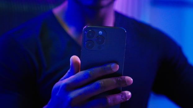 Close up male hands night dark room browsing mobile phone app online bet casino futuristic gamer unrecognizable African American man male guy smartphone internet play game innovation futurism neon photo