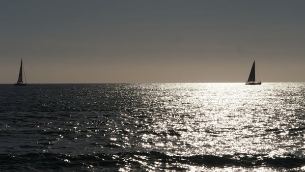 Two sailboats sailing away on calm ocean at sunset with sparkling water photo