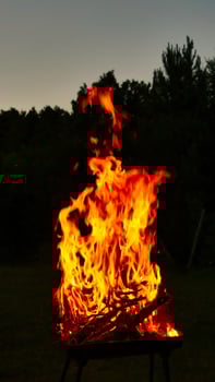 Burning firewood making large flames in a barbecue grill at dusk photo