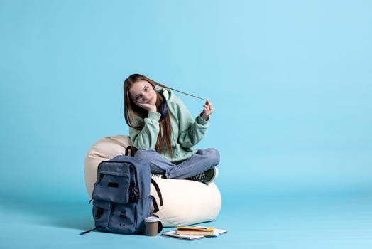 Portrait of bored person sitting on beanbag, playing with hair, isolated over studio background. Disinterested teenager resting at home surrounded by school supplies, wasting time photo