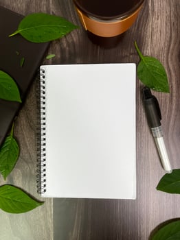 Still life photography blank notebook on wooden table with a cup of coffee, plant, leaf on table photo