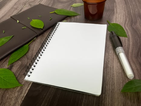 Still life photography blank notebook on wooden table with a cup of coffee, plant, leaf on table photo