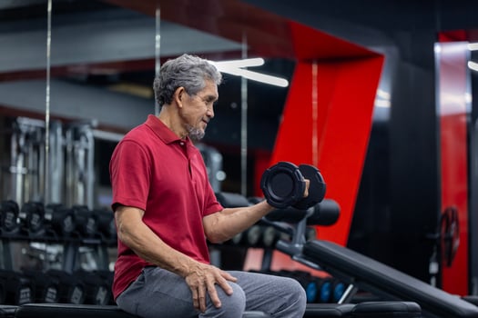 Asian senior man wearing sportswear doing weight lifting on single dumbbell to gain bicep muscle while having exercise training in the gym for longevity and retirement concept photo