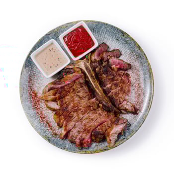 Sliced grilled t-bone steak with sauces on plate, top view photo