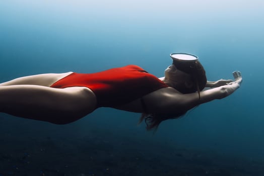 Young gorgeous woman freediver in red swimwear swims underwater in deep ocean. Sexy woman freedives. photo