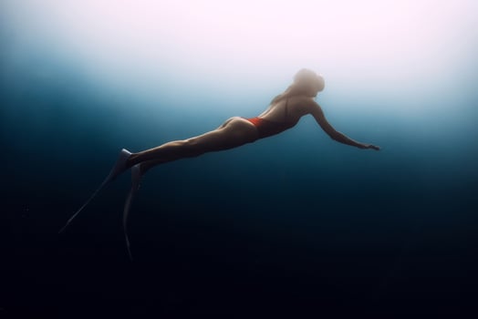 Gorgeous female freediver swims underwater in deep blue ocean. Sexy woman silhouette undersea. photo