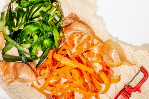 Vegetable peelings on wrapping paper and vegetable peeler on white table photo