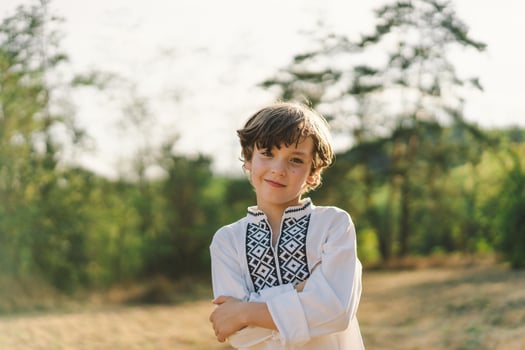 A boy smiles confidently while standing in a sunlit field, wearing a traditional embroidered shirt photo