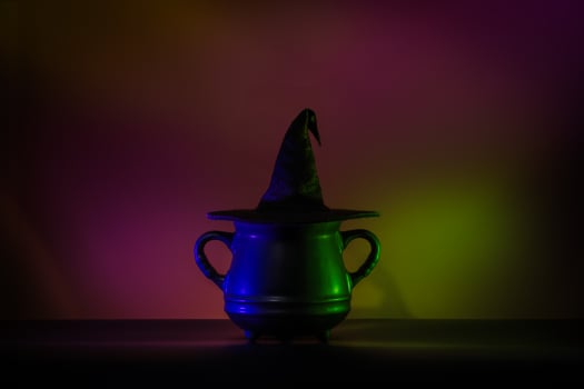 Creative minimalist Halloween background image featuring a witch hat on a cauldron in lowkey neon lighting. Perfect for modern and trendy Halloween designs. photo
